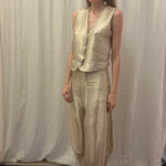 Woman in a gold dress standing in front of a white curtain with a patterned rug on the floor.